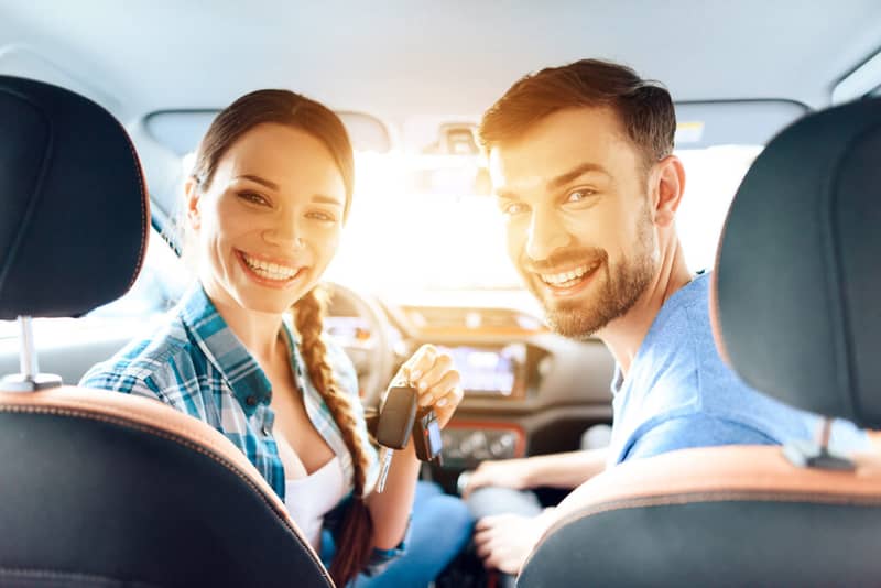 Happy couple with their rental car keys inside the vehicle