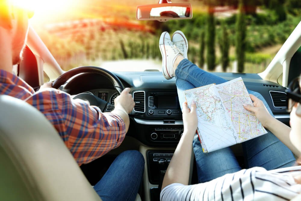 Couple on a scenic road trip with a map inside a rental car